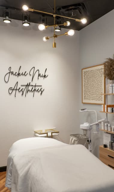 Jackie Nack Aesthetics esthetician suite at Cosmo Salon Studios, with a facial bed, gold light fixture and skin care devices