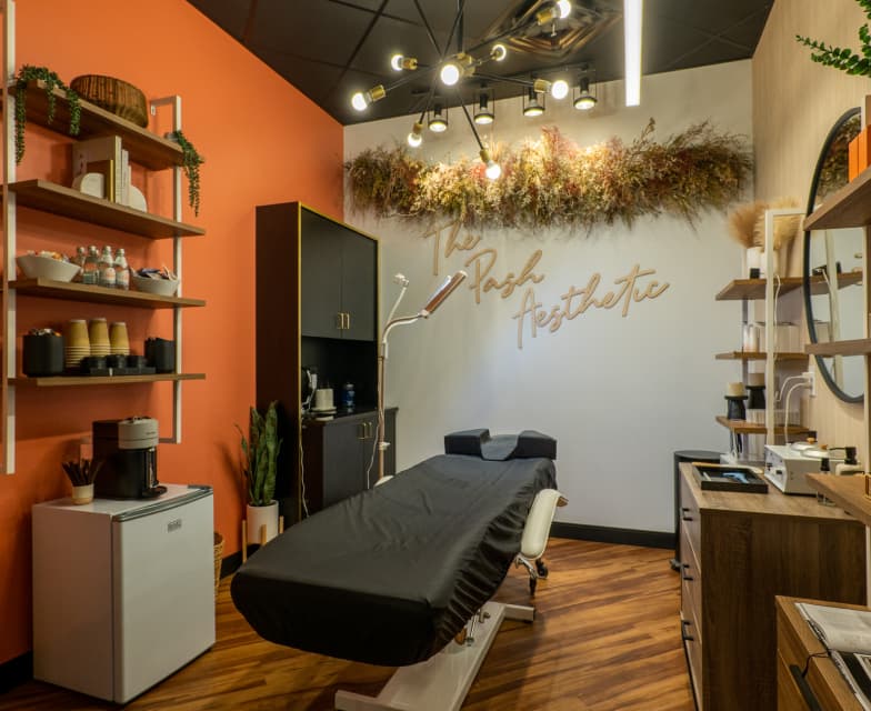 The Pash Aesthetic esthetician suite at Cosmo Salon Studios, with a treatment bed, orange accent wall and open shelving